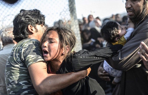 Syrische vluchtelingen proberen door een hek van prikkeldraad te breken