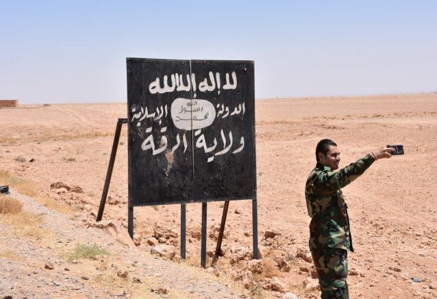 Een Syrische soldaat neemt een selfie met een bord van ISIS